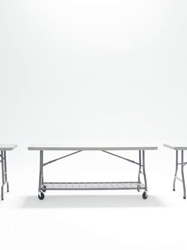 A woman places a folding table from Hallgruppen next to two already set-up folding tables in a white room. The tables have metal legs and are designed for easy transport and storage.