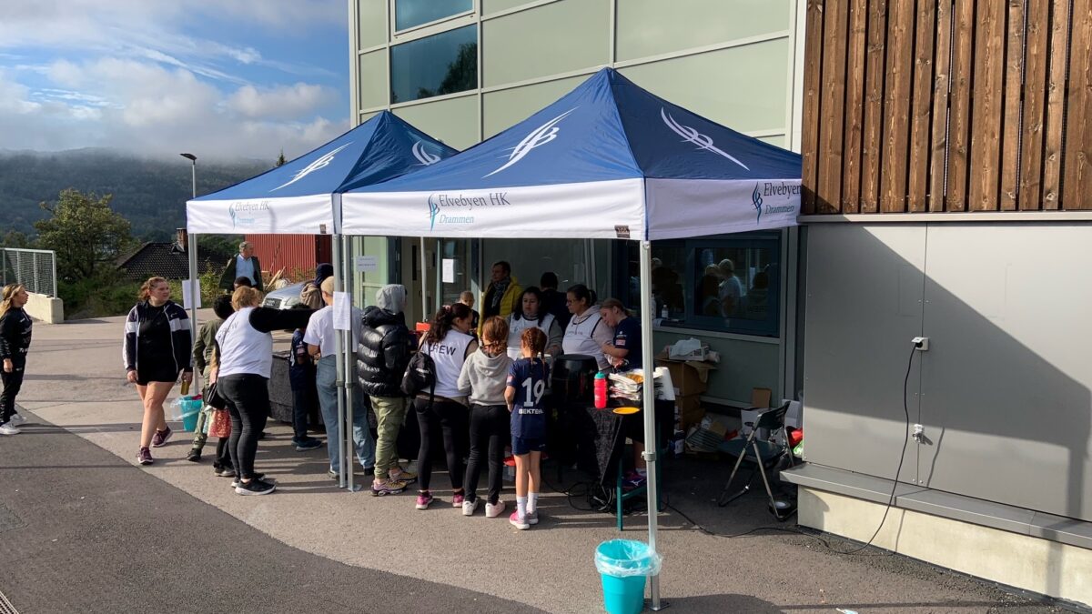 Namiot reklamowy od Hallgruppen z brandingiem Elvebyen ILK na wydarzeniu plenerowym. Namiot chroni uczestników i sprzęt przed warunkami atmosferycznymi.