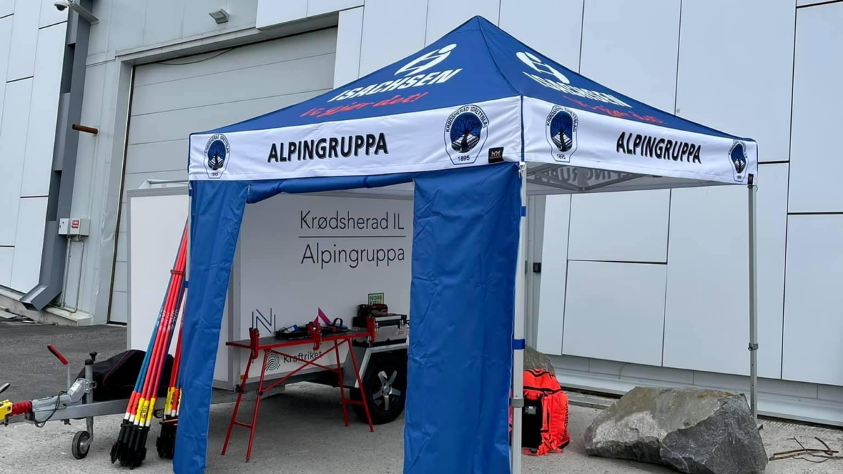 Hallgruppen dostarczył namiot reklamowy dla Krødsherad IL Alpingruppa, ustawiony przed białym budynkiem. Namiot posiada nadrukowaną nazwę i logo klubu.