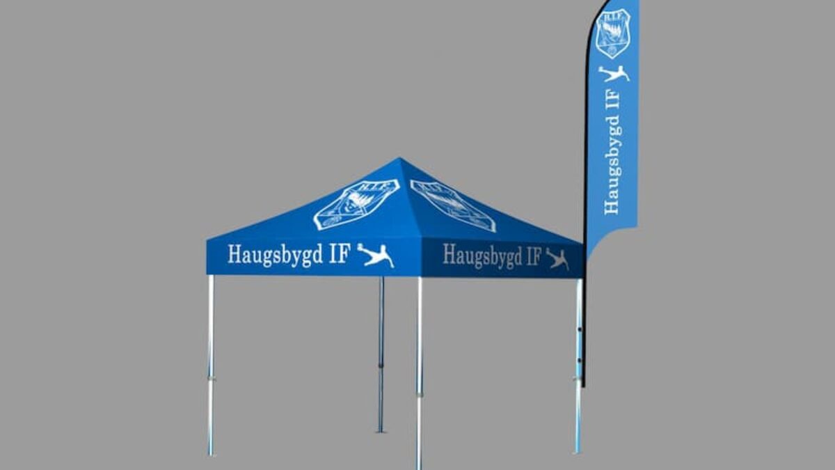 Niebieski namiot reklamowy z brandingiem Haugsbygd IF stoi w strefie wystawowej. Namiot posiada pasującą flagę i jest wykorzystywany na wydarzenia sportowe.