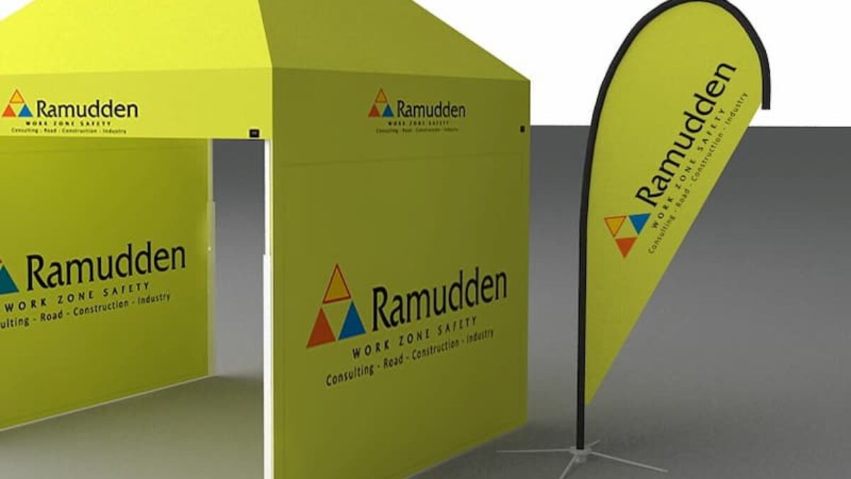 Żółty namiot reklamowy od Ramudden, rozstawiony z pasującą flagą po boku. Namiot ustawiony jest na szarej powierzchni. Hallgruppen dostarczył ten namiot.