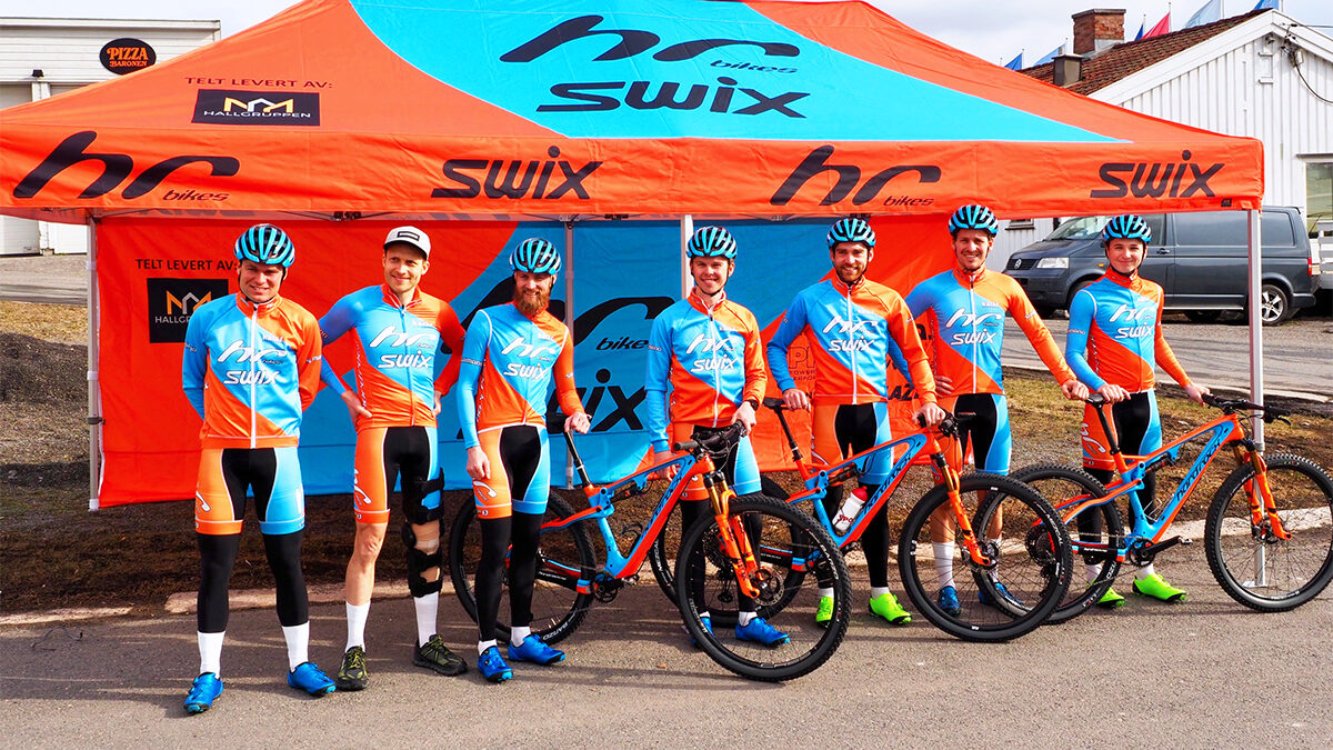 Hallgruppen dostarczył namiot reklamowy z brandingiem HC bikes. Grupa kolarzy w kolorowych strojach stoi przed namiotem ze swoimi rowerami górskimi.
