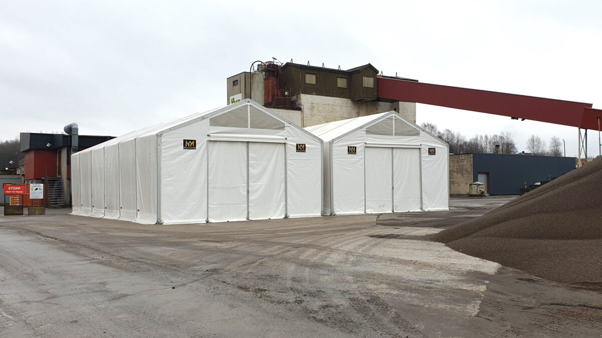 Biała hala przemysłowa od Hallgruppen na terenie przemysłowym, otoczona budynkami i maszynami.