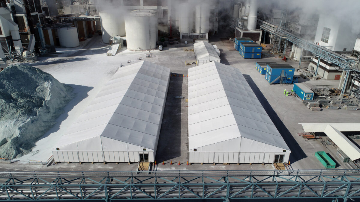 Dwie białe hale przemysłowe od Hallgruppen na terenie przemysłowym, otoczone rurami i budynkami.