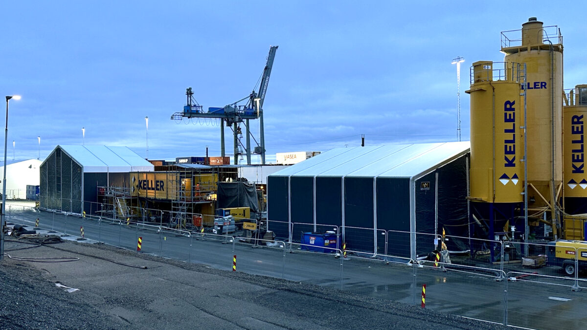 Duża hala przemysłowa od Hallgruppen w trakcie montażu na placu budowy, z sekcją podnoszoną za pomocą dźwigu.