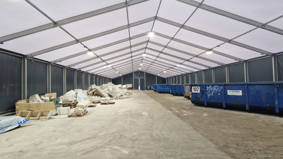 Wnętrze hali przemysłowej od Hallgruppen, z przestronną powierzchnią wypełnioną materiałami budowlanymi i kontenerami.