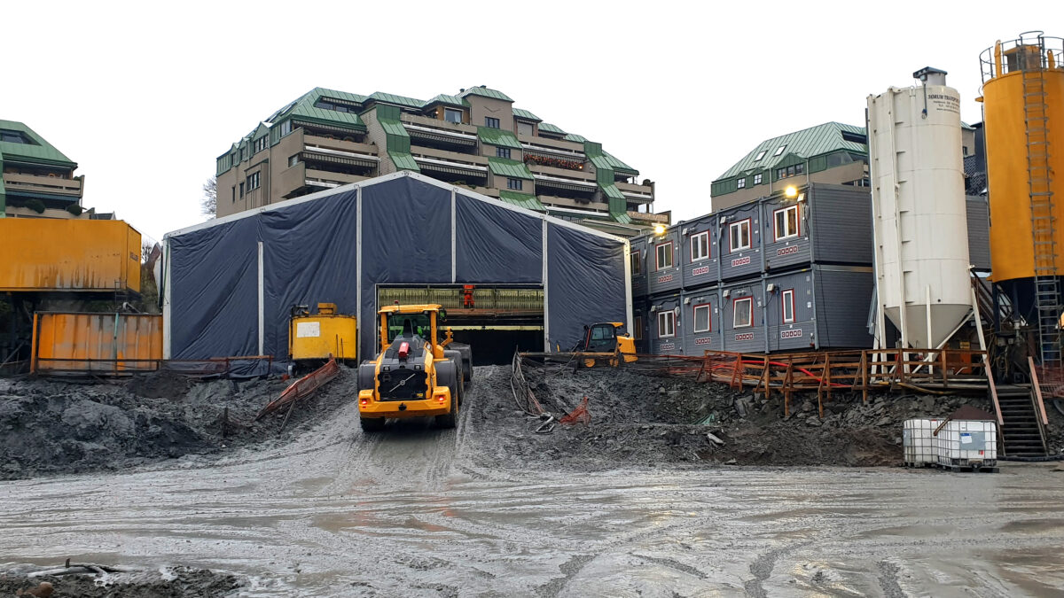 Hala przemysłowa od Hallgruppen na terenie fabryki, otoczona sprzętem budowlanym i kontenerami.