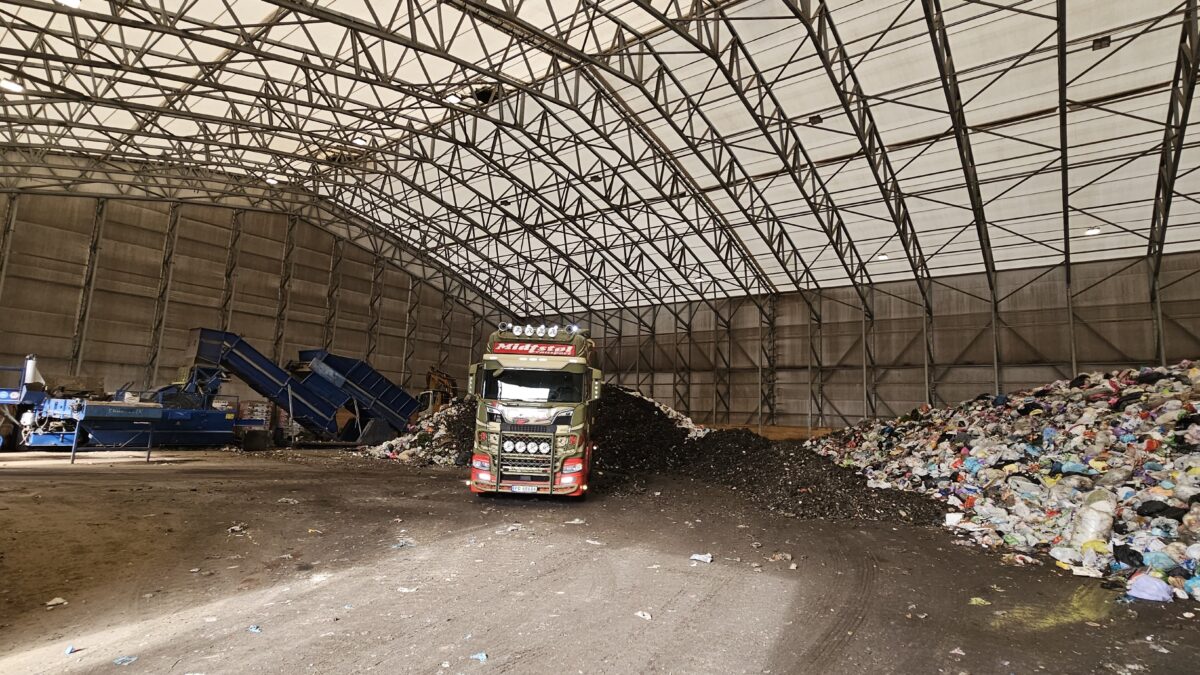 Hallgruppen zaprojektował przestronną halę do recyklingu z hałdami odpadów wewnątrz, gdzie ciężarówka pracuje nad przemieszczaniem materiału.